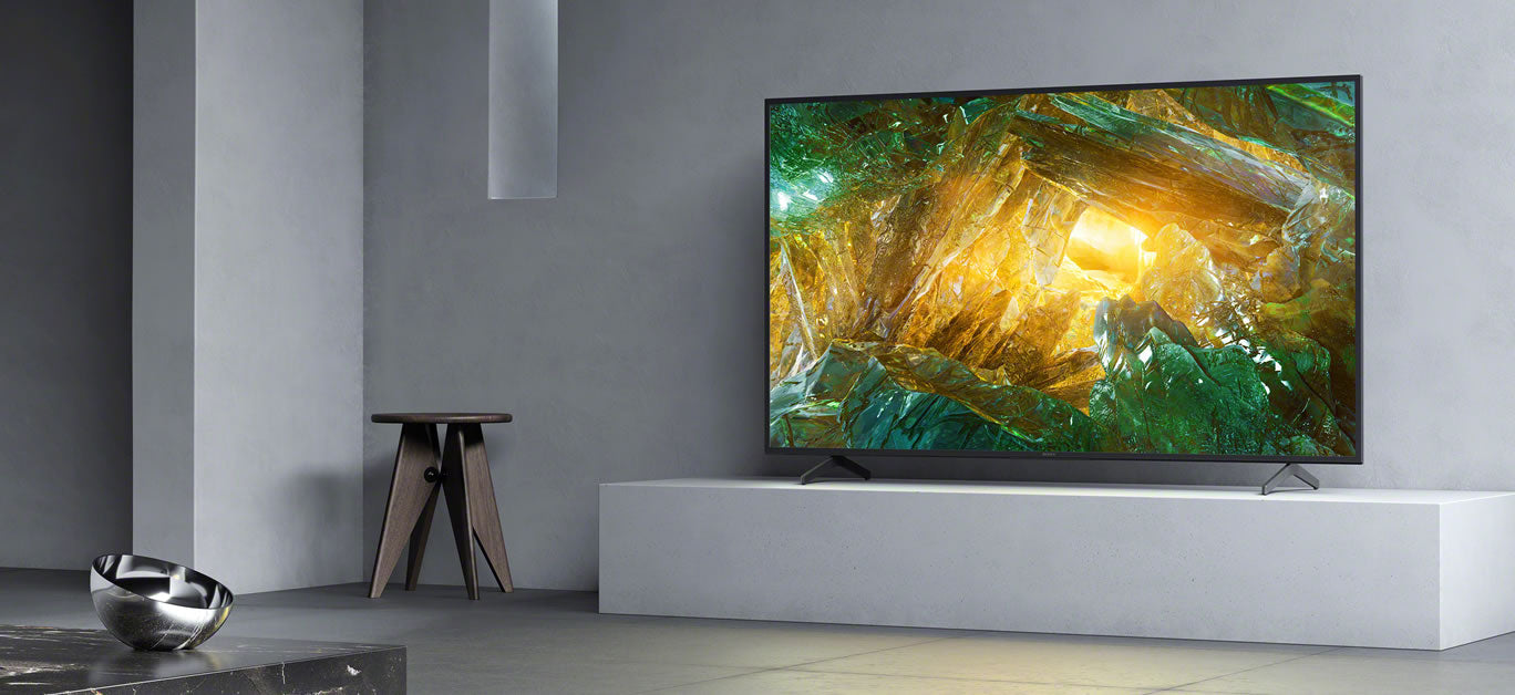 A large 4K TV in a minimalist grey living room, showing the scale of the screen against the seating area