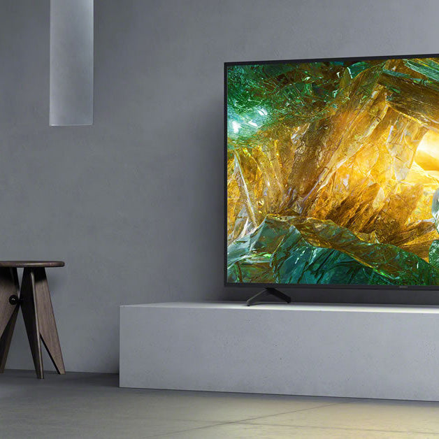 A large 4K TV in a minimalist grey living room, showing the scale of the screen against the seating area