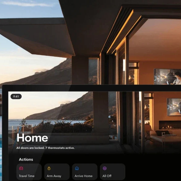 A wall-mounted smart home touchscreen controlling lighting, security and audio in a modern hillside home at sunset.